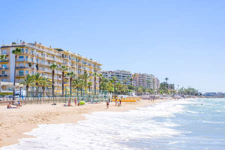 CANNES, FRANCE - JUNE 29, 2017: Daylight view to beachline with people relaxing on sand with traces. Big hotel buildings and bright blue sky on background. Waves on seashore. Place for textのeditorial素材