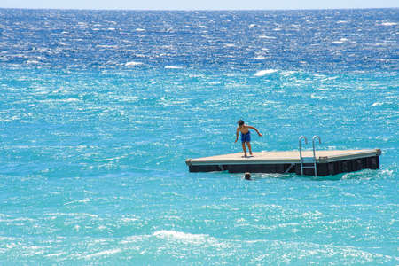 CANNES, FRANCE - JUNE 29, 2017: Daylight closeup view to a swimming woman and man preparing for jumping in blue water from platform. Place for text, negative copy spaceのeditorial素材