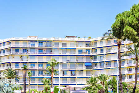 Daylight view to yellow hotel building and green trees. Bright blue clear sky. Negative copy space, place for text. Cannes, Franceの写真素材