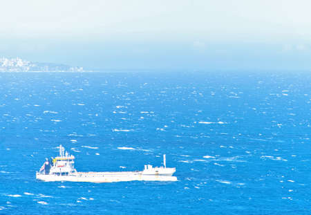 Daylight closeup view to cargo ship cruising on water. Mountains and bright sky on background. Negative copy space, place for text. Monte Carlo, Monacoの写真素材