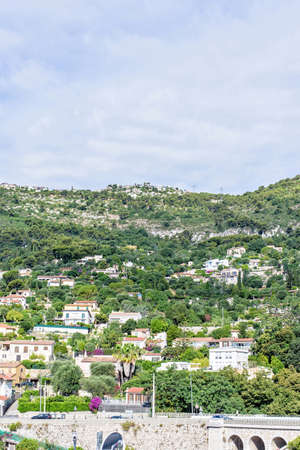 Daylight sunny view to city buildings and green trees on mountains. Parked cars and people walking. Cloudy sky on background. Negative copy space, place for text Monte Carlo, Monacoの写真素材
