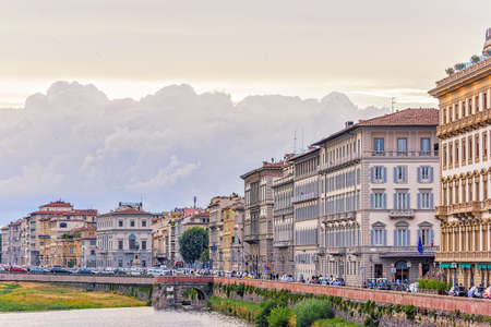 Daylight panoramic cloudy day view to Arno river with sunset reflections and cars riding on bridge. People walking on streets, Florence, Italyの写真素材