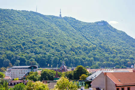 Daylight sunny view to Brasov sign in Romania. Green trees on mountains and buildings roof. Bright...
