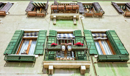 Daylight view from bottom to historic architecture building with green facade and balconies. Bright blue sky with clouds. Murano Island, Venice, Italyの写真素材