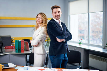 Men and woman business partners posing for a photo in the office. Table with blueprints on...