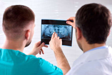Two caucasian male dentists analyzing x-ray in dental cabinet. Close-up shot