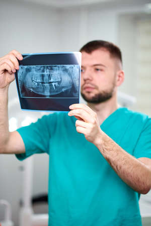 Caucasian male dentist holding xray in hands and smiling. Looking towards cameraの写真素材