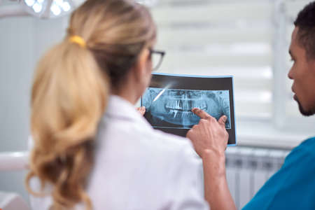 Caucasian female dentist explaining to african male rookie how to analyze the x-rayの写真素材