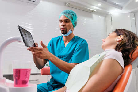 African male dentist explaining x-ray to the patient sitting in the chairの写真素材