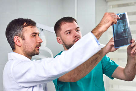 Two caucasian male dentists analyzing x-ray in dental cabinet. Close-up shot