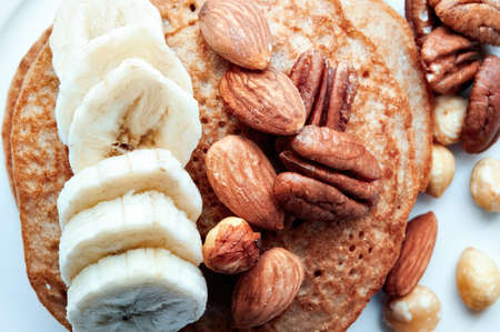 Pancakes with nuts and sliced bananas on a white dishの写真素材