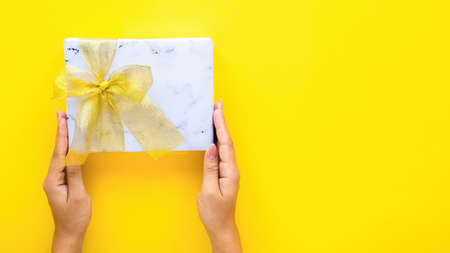Female hands hold a gift box on yellow background. Holiday concept. Top viewの写真素材