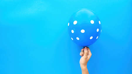 Female hand holds a balloon with white circles on blue background. Holiday concept. Top view