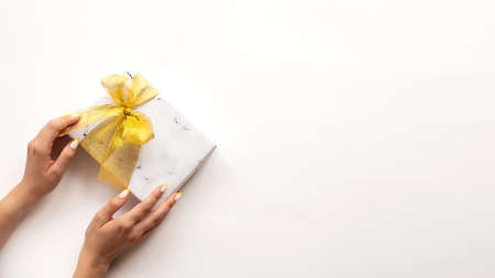 Female hand holds a gift box with golden tape on white background. Holiday concept.