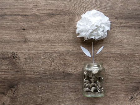 A glass can with metal coins and a flower growing up in it. Wooden background. Top viewの写真素材
