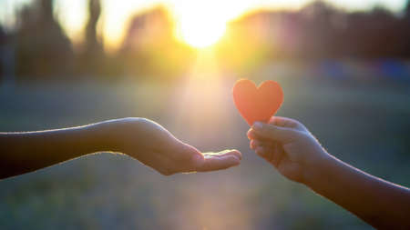 A kid is giving a man a red heart, setting sun. Love concept