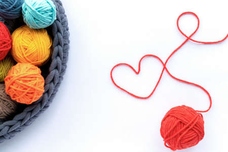 Multicolored balls of yarn in the knitted couch and one red ball making a heart. Top view