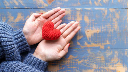 Female hands holding a handmade knitted red heart. Top viewの写真素材