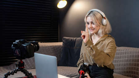 Young content creator blonde smiling girl with her laptop on the table. Filming herself using a...