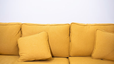 Yellow canvas sofa with two pillows on it and white wall on the background