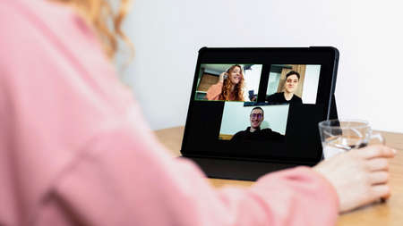 Young ginger girl with headphones talking to her friends in video conference. Group of young people working from homeの写真素材