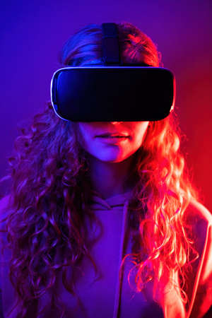 Young girl in virtual reality glasses with blue and red illumination in the room. Entertainment at...