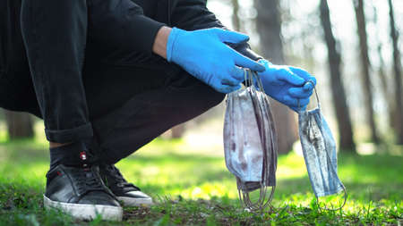 Man in medical gloves picking up dirty medical masks from the ground in a park. Pollution ideaの写真素材