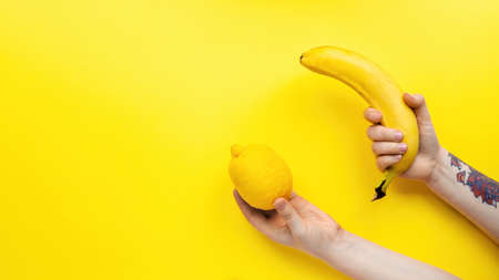 Female hands holding lemon and banana on yellow backgroundの写真素材