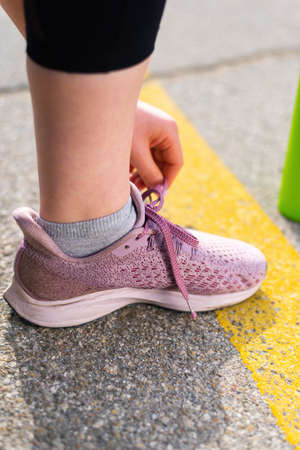 Young woman tying her shoelaces at outdoors training, roadの写真素材