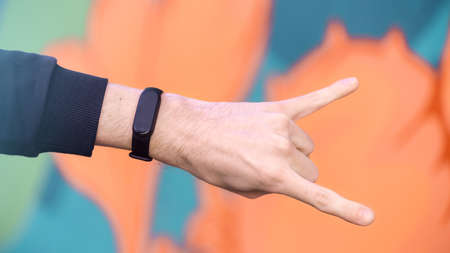 A male hand showing rock sign with fitness bracelet on it, multicolored background