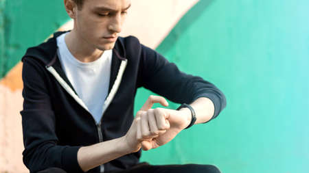 Young caucasian man is on his fitness bracelet on multicolored background