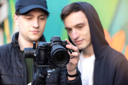 Two caucasian men looking into the camera screen on a steadicam, colored background