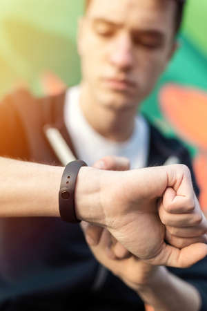 Young caucasian man is on his fitness bracelet on multicolored background