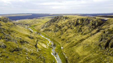 Gorge in the hills of Moldova with floating river, cloudy sky, fields on the background, view from the droneの写真素材