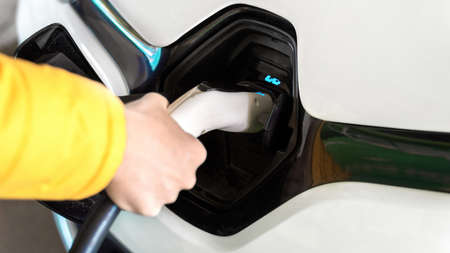 Man plugging in charger into an white electric carの写真素材