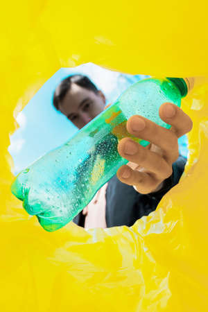 Man throwing a green plastic bottle into a trash can. View from inside the canの写真素材