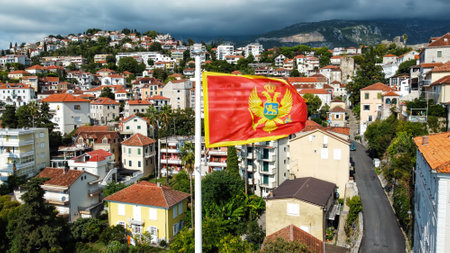 Aerial drone view of the national flag of Montenegro. Town with residential buildings and greenery on the backgroundの写真素材