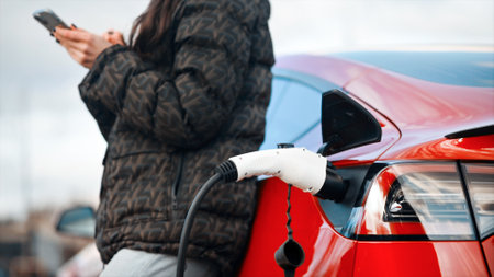 Close view of a woman using smartphone near her charging red electric carの写真素材