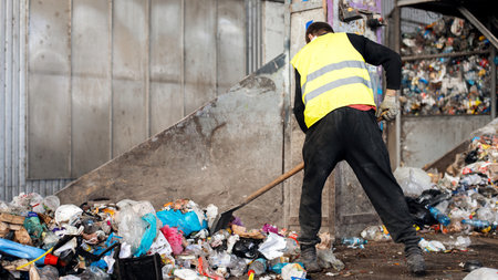 Worker pushing garbage to a conveyor belt at waste sorting plantの写真素材