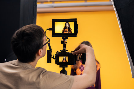 View of a professional photographer shooting a young woman using a camera with external display, yellow backgroundの写真素材
