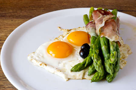 Asparagi with fried egg brown and black olives over wooden tableの写真素材