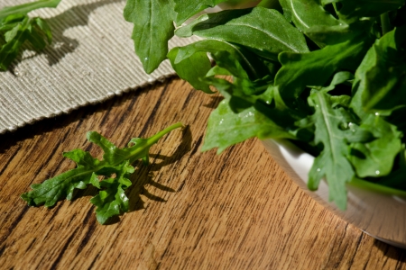 bowl of fresh green, natural arugula on wooden table and sun morning lightの写真素材