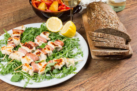 grilled chicken on bamboo skewers with wine, red peppers and integral bread on wooden tableの写真素材