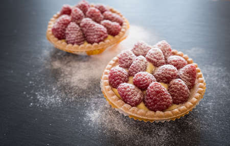 Raspberry tartlets with custard and powdered sugar on the dark backgroundの写真素材