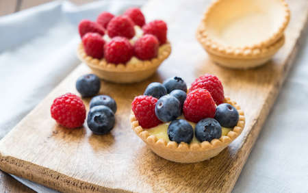 Homemade custard tartlets with raspberries and blueberries on the wooden table, close upの写真素材