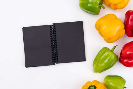 Black notebook with colorful pepper top view on a white background