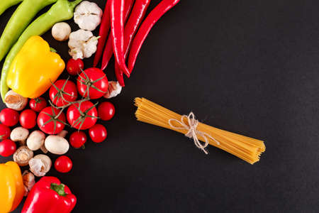 Fresh vegetables and raw spaghetti top view on black backgroundの写真素材