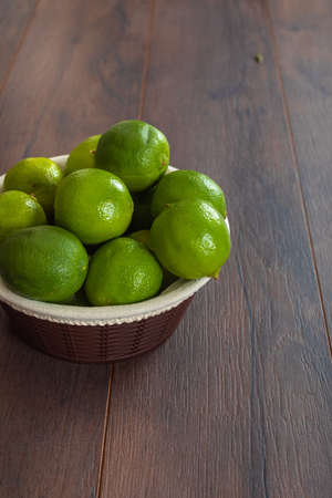 Green lemons in basket on brown tableの写真素材