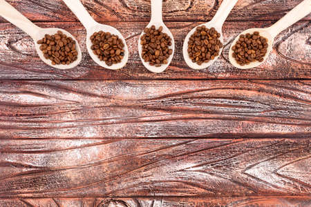 Roasted coffee beans in spoons row by row on wooden textureの写真素材