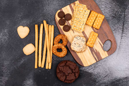 Top view, different cookies on wooden board on dark background
